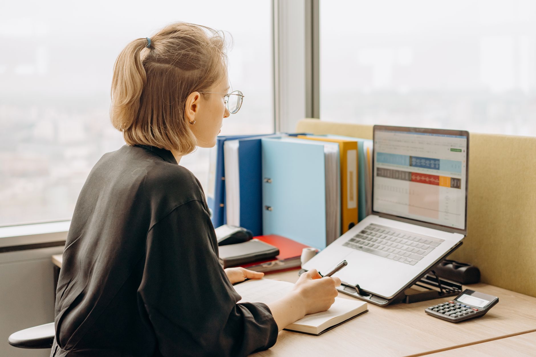 A side view of a professional woman working on a laptop with spreadsheets in a modern offi