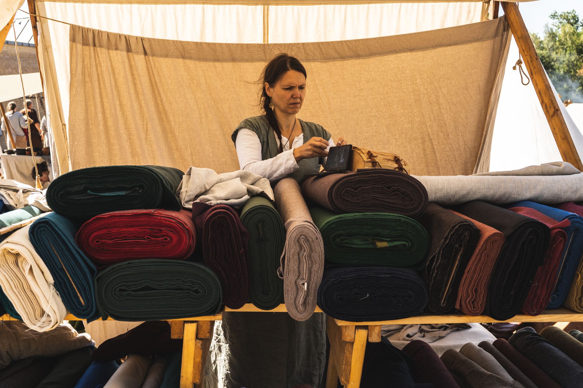 A woman sells colorful fabrics at an outdoor market, engaging in business activities.